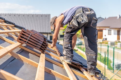 Is Roofing Business Profitable? 7 Roofer placing roof tiles on wooden frame of house roof while considering the question is roofing business profitable.
