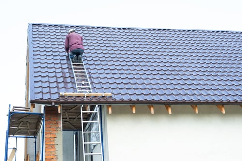 Is Roofing Business Profitable? 1 Roofer on ladder fixing tiled roof on house, showing real work behind question is roofing business profitable.