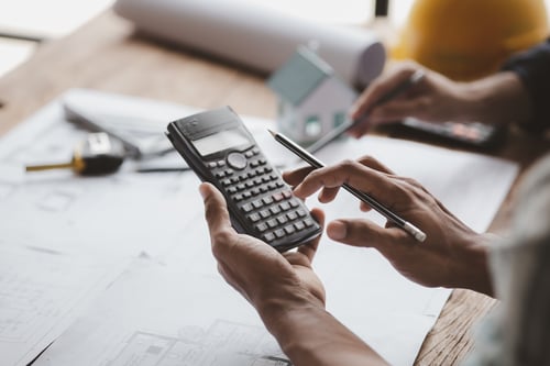 Is Roofing Business Profitable? 3 Person using a calculator over building plans while considering the question is roofing business profitable.
