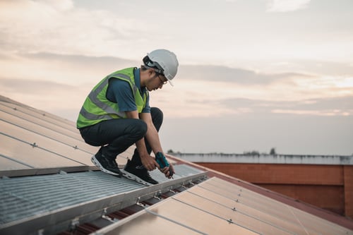 Is Roofing Business Profitable? 4 Roofer installing metal roof panels at sunset while reflecting on the question is roofing business profitable.