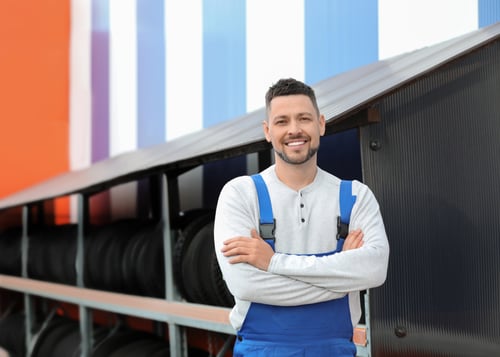 Is Roofing Business Profitable? 9 Confident roofing contractor standing with folded arms beside metal roofing panels, reflecting success behind the question is roofing business profitable.