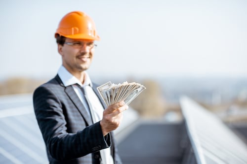 Is Roofing Business Profitable? 2 Businessman in hard hat holding cash on a rooftop, symbolising the question is roofing business profitable.